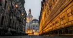 Narrow street in Dresden, Germany, flanked by historic buildings with illuminated windows and a distant dome visible at dusk.