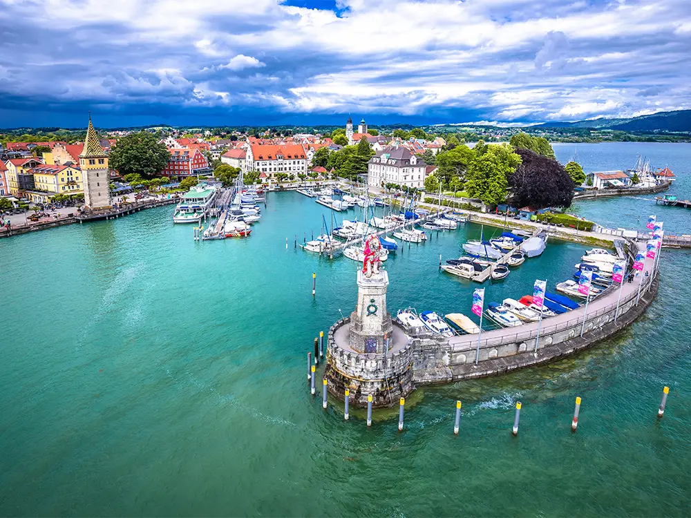 Aerial view of Lindau harbor with turquoise water, boats, and the Bavarian lion statue at Lake Constance.