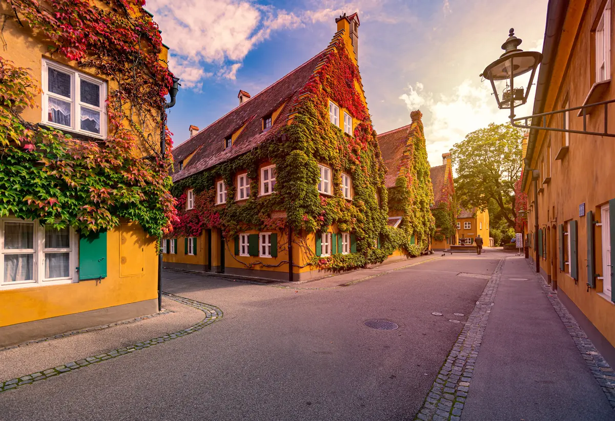 Street view of charming, ivy-covered houses in Augsburg at sunset, with cobblestone roads and a lantern on the right.