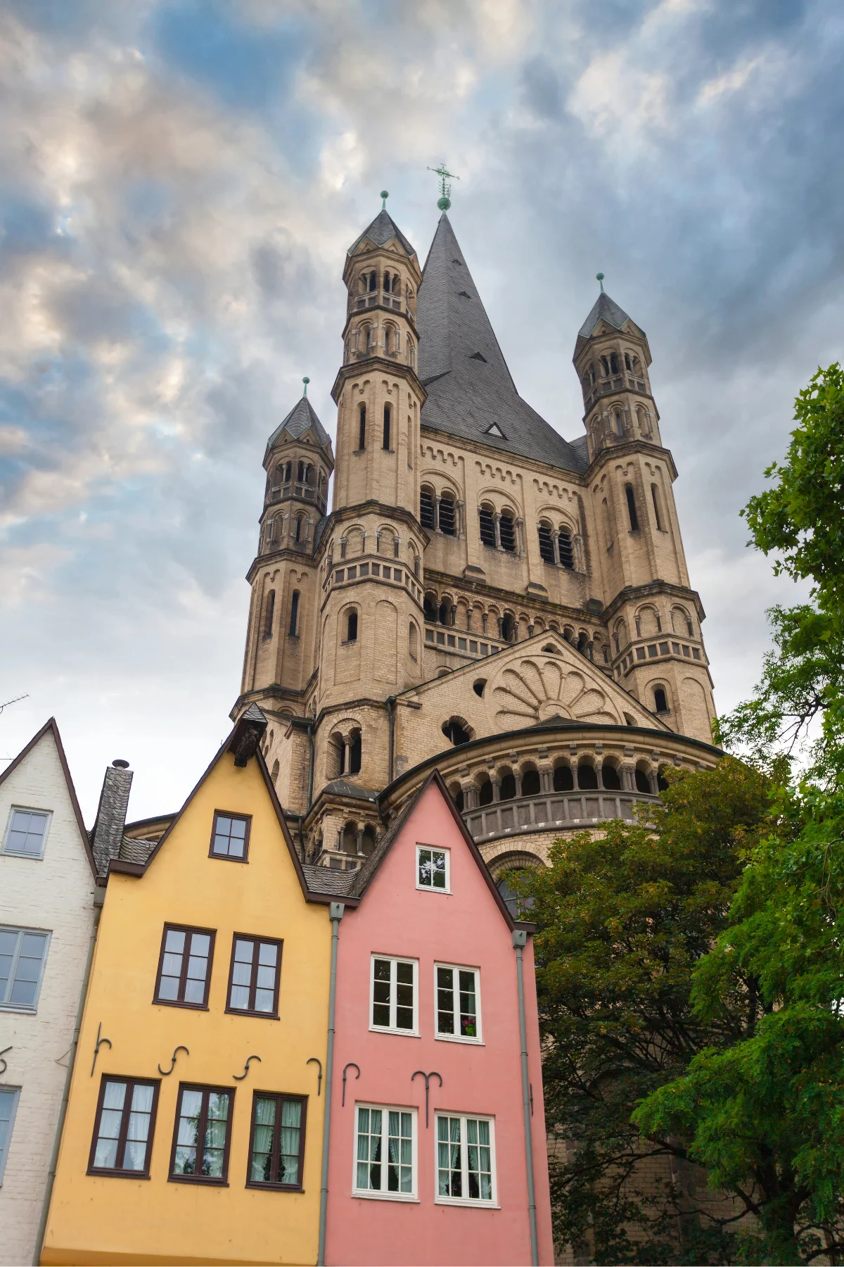 Old church tower rising up behind multi-coloured houses in Cologne.
