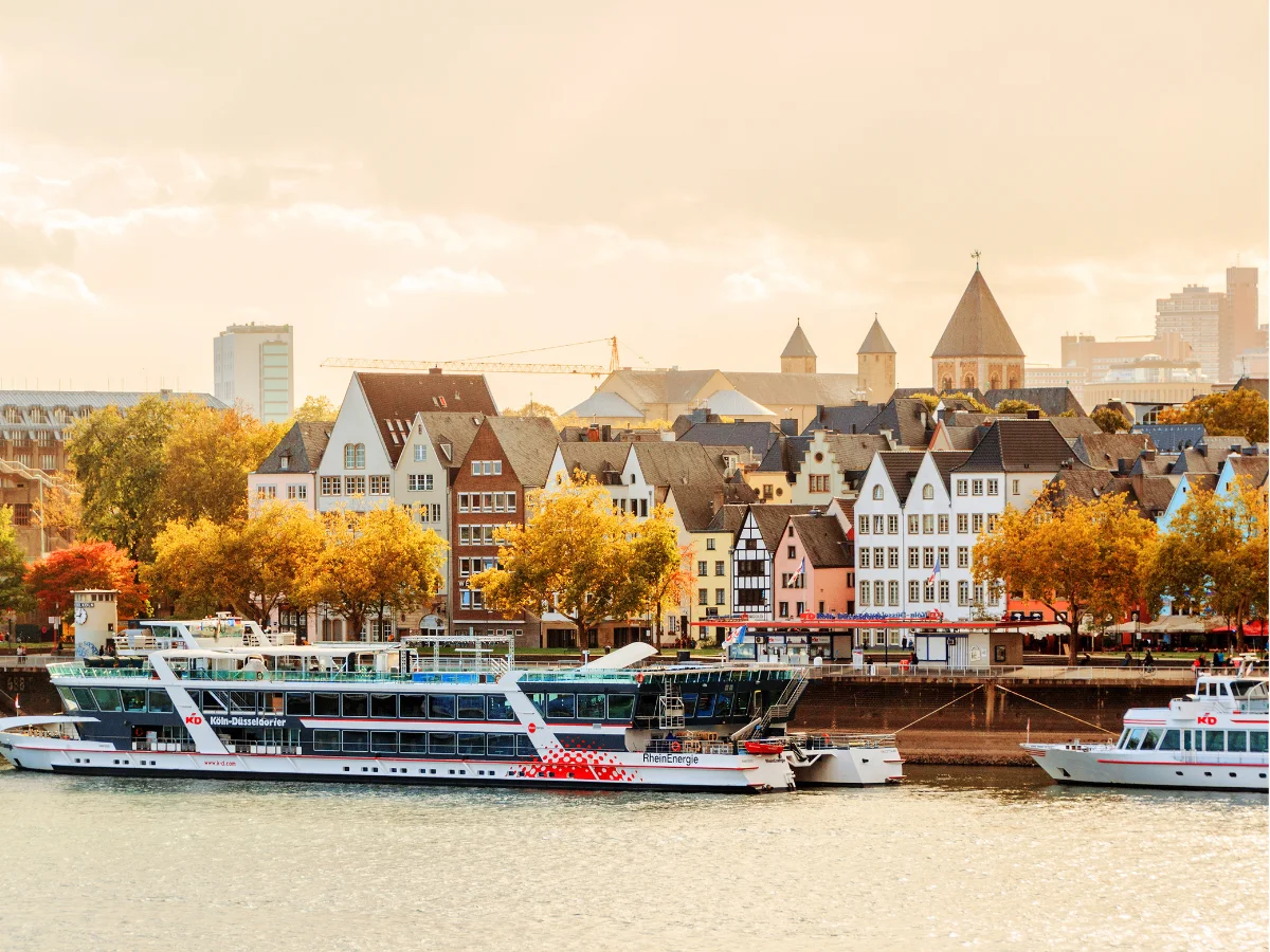 River in Cologne with boat and houses surrounded by trees in an autumn sunset.
