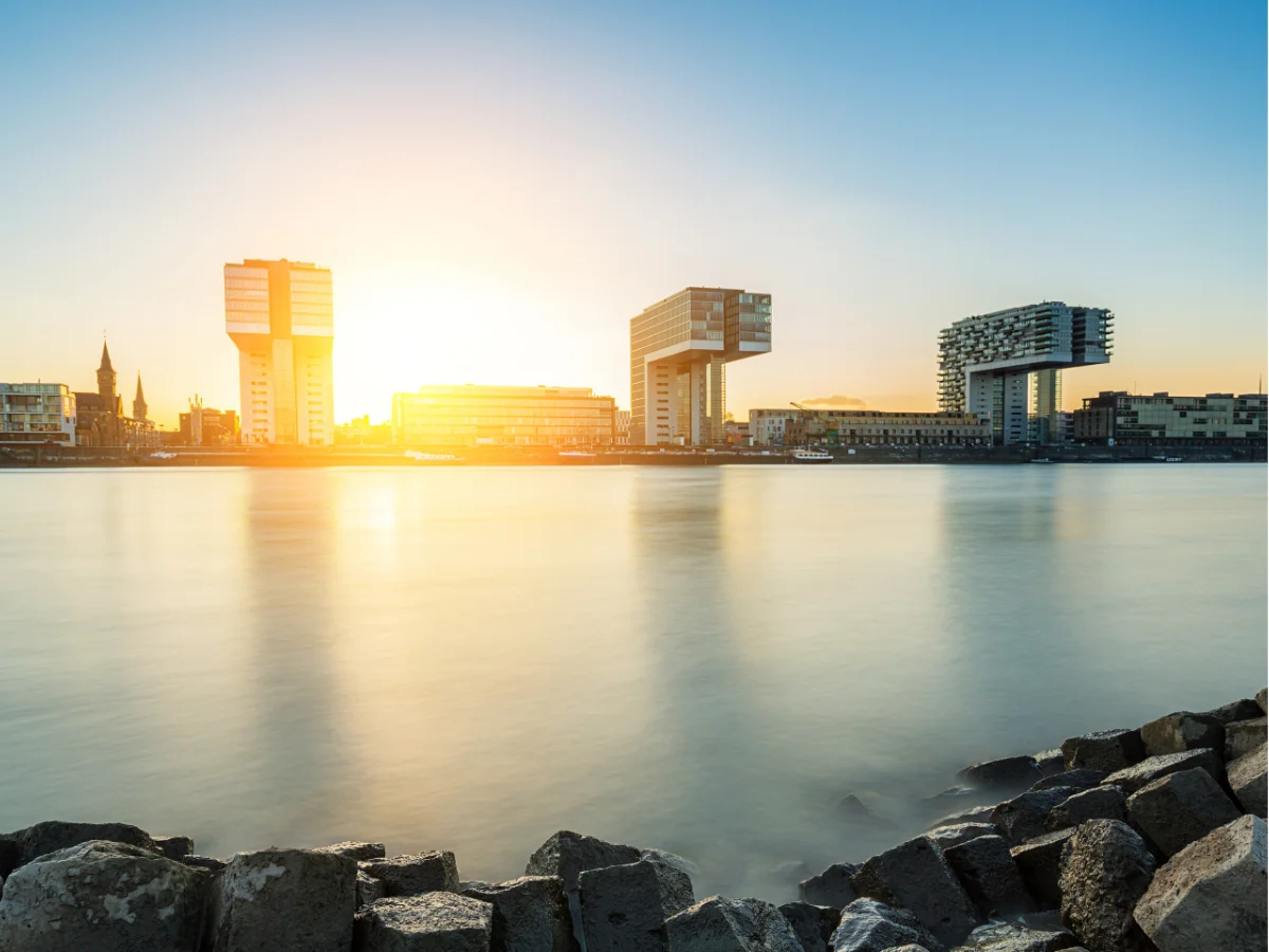 Three buildings overhanging the river in Cologne at sunset.