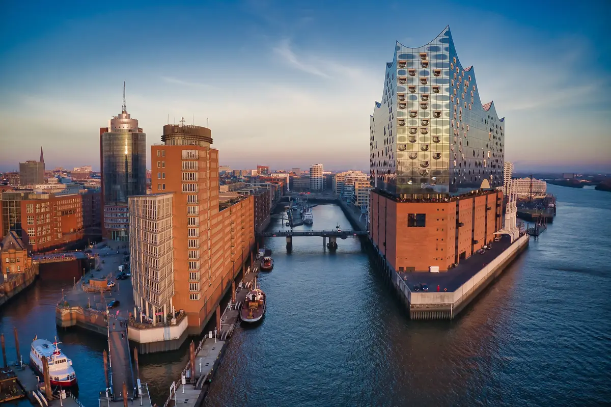 Aerial view of the Elbphilharmonie concert hall in Hamburg, Germany, surrounded by water and adjacent buildings at sunset.