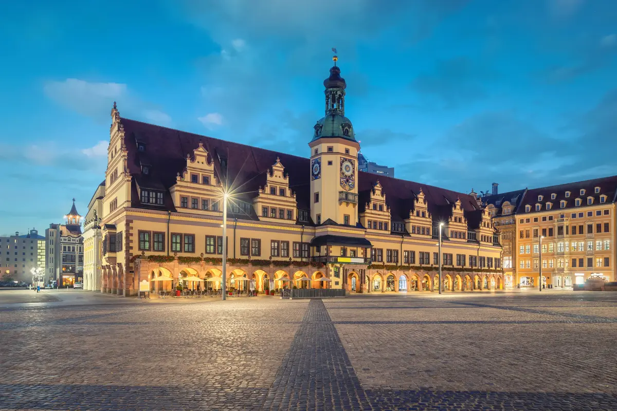 Historic building with a clock tower in a spacious plaza at dusk, under a clear sky.