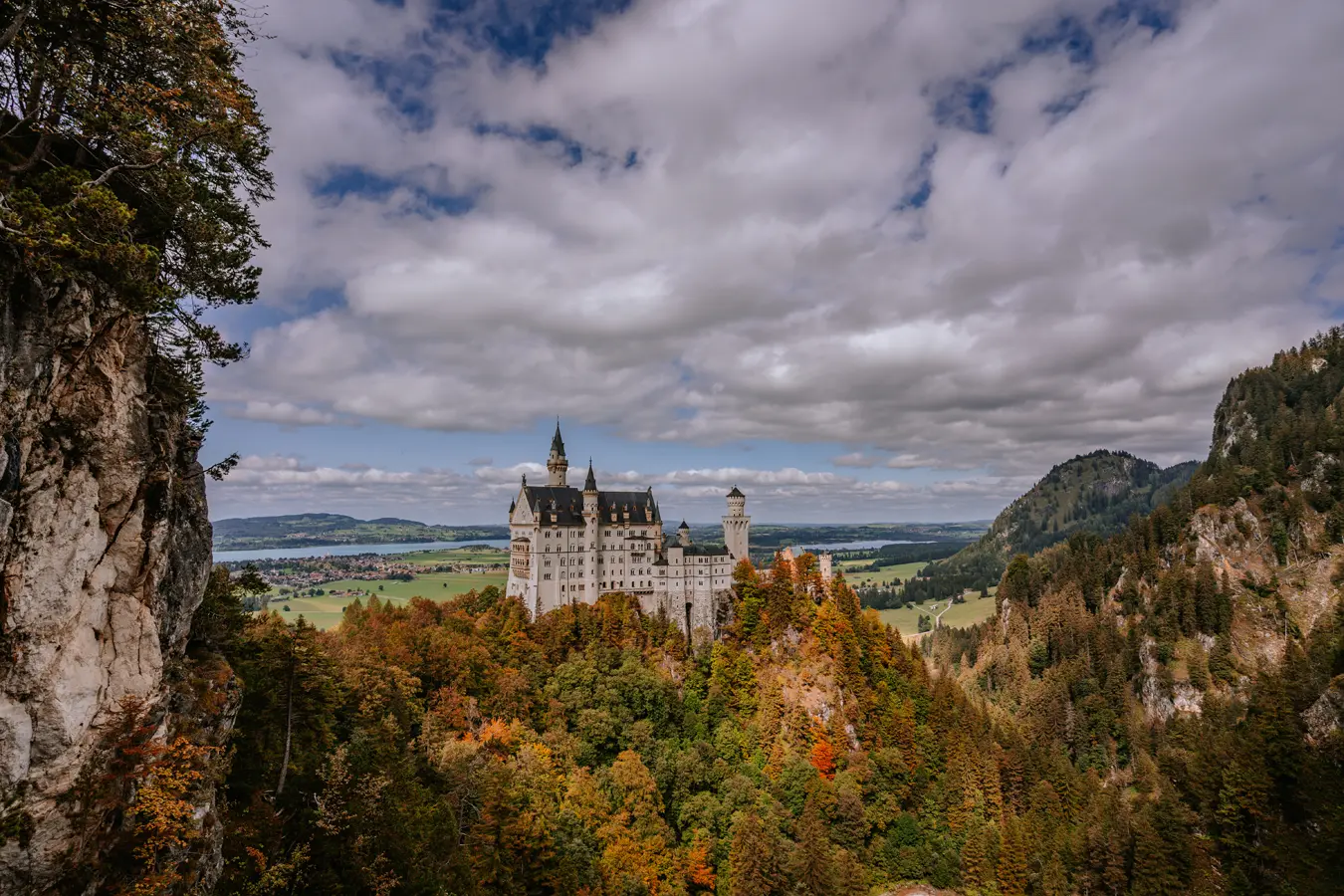 Neuschwanstein Castle with mountains in the background and moon shining through clouds.
