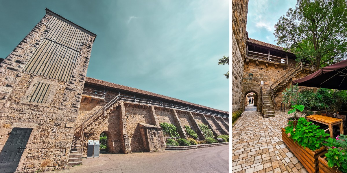 A narrow, tall stone building on the left and a medieval courtyard with a cobblestone path, planters, and wooden tables on the right, both under a clear sky in Rothenburg, Germany.