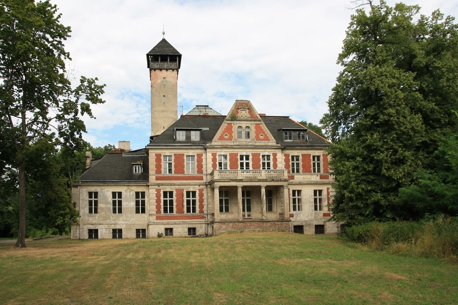 Schulzendorf Schloss, a large, historic building with a tower and ornate façade, surrounded by trees, under a partly cloudy sky.