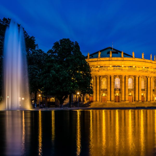 Fountain by pond in front of the lit up pillared rotunda of the Staatstheater, Stuttgart