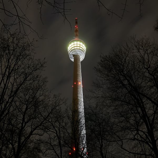 Stuttgart TV Tower lit up at night, trees in front