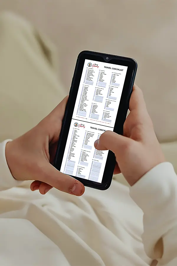 A person holds a smartphone displaying a travel checklist, viewed from over the shoulder.