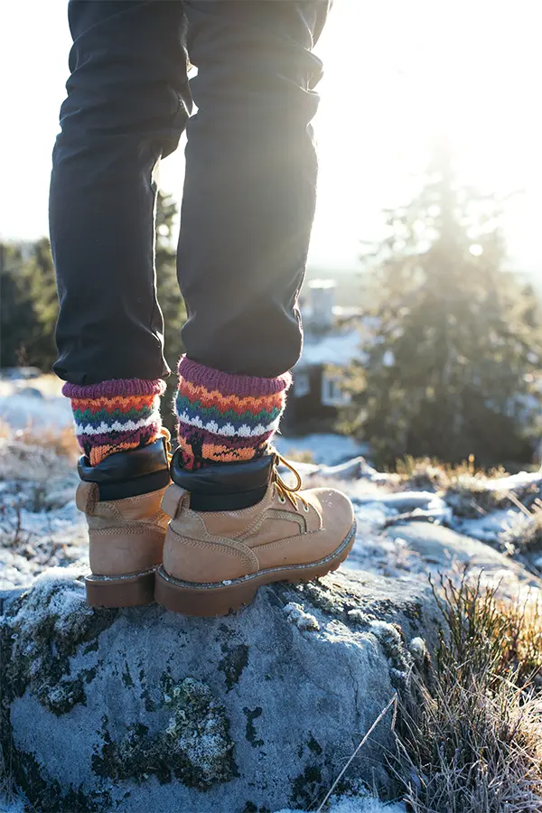 Person standing on a rock wearing hiking boots and colorful socks in a frosty landscape with trees in the background.