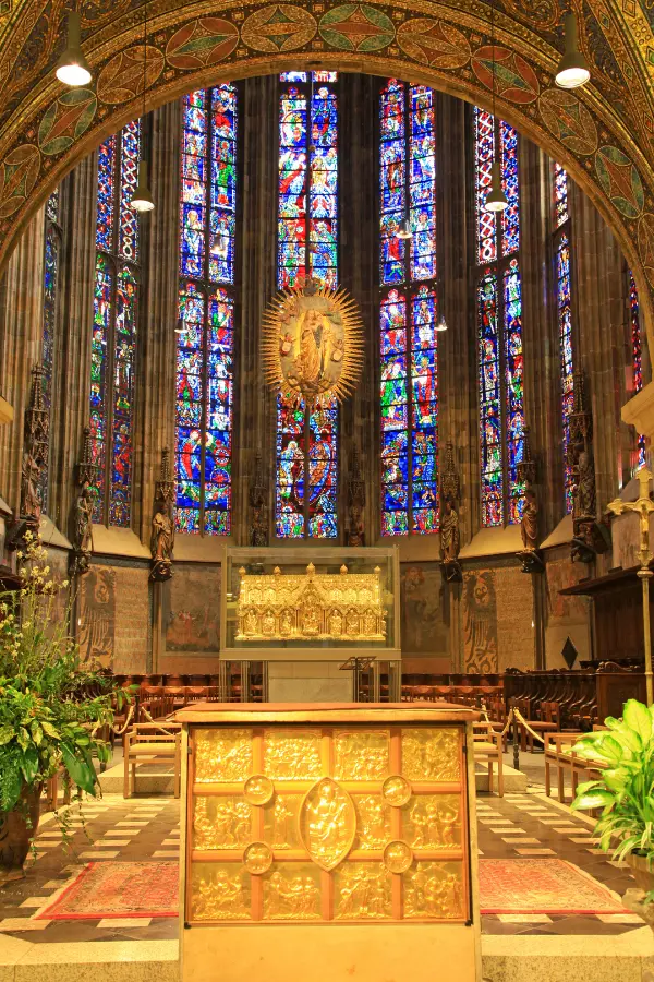 Interior of Aachen Cathedral featuring a golden altar, ornate stained glass windows, and decorative arches.