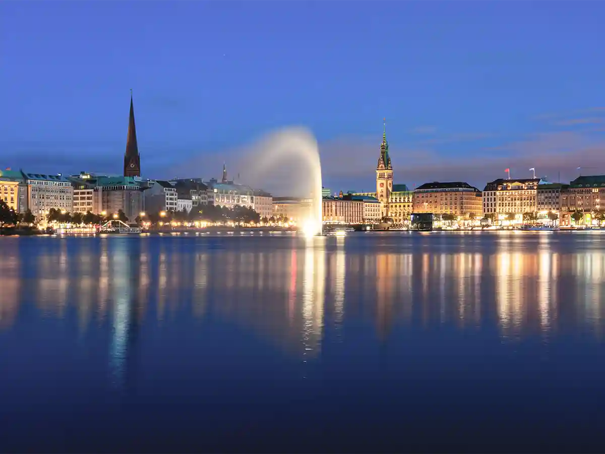 Night view of the Binnenalster lake in Hamburg, Germany, with city buildings, illuminated fountain, and reflections on the calm water. Night view of the Binnenalster lake in Hamburg, Germany, with city buildings, illuminated fountain, and reflections on the calm water.