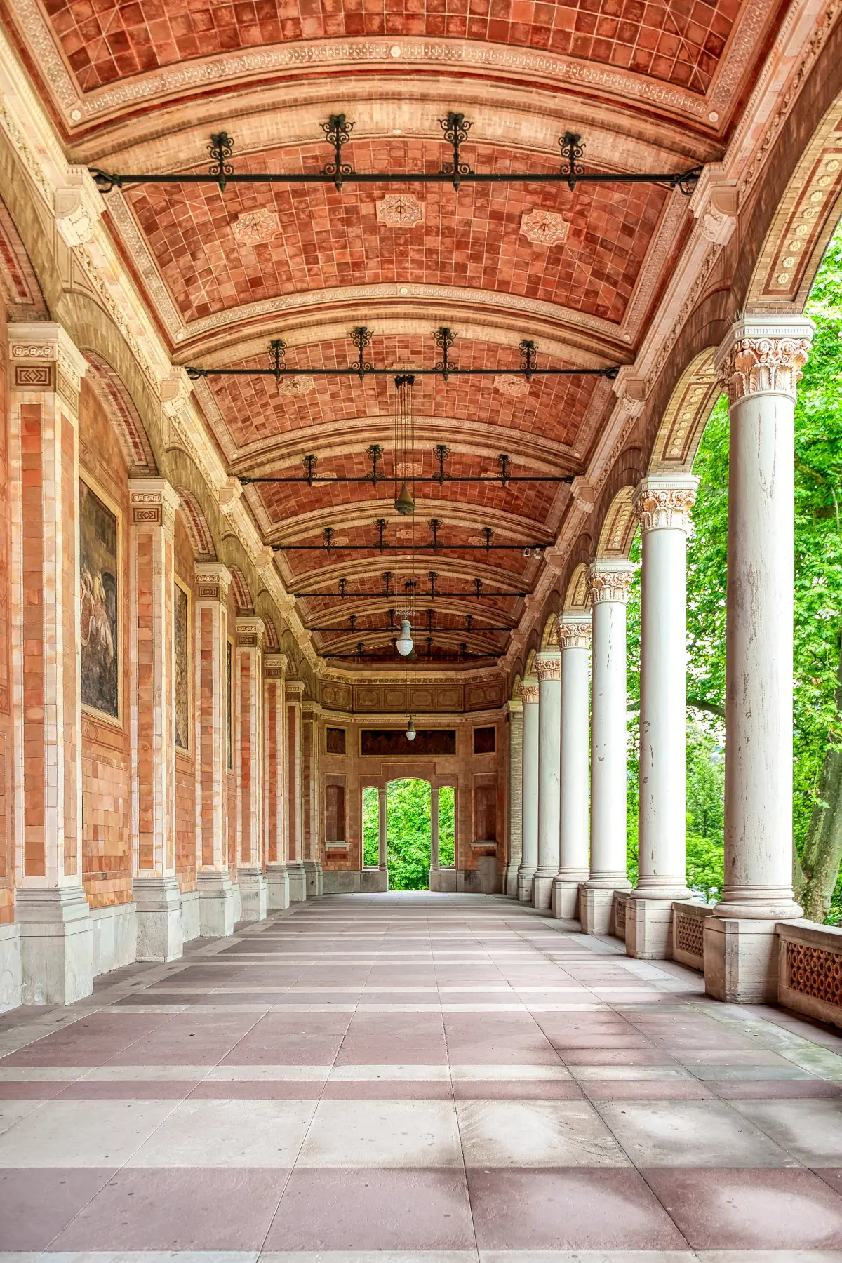  Covered walkway with a red-tiled arched ceiling, stone columns, and open windows overlooking greenery.