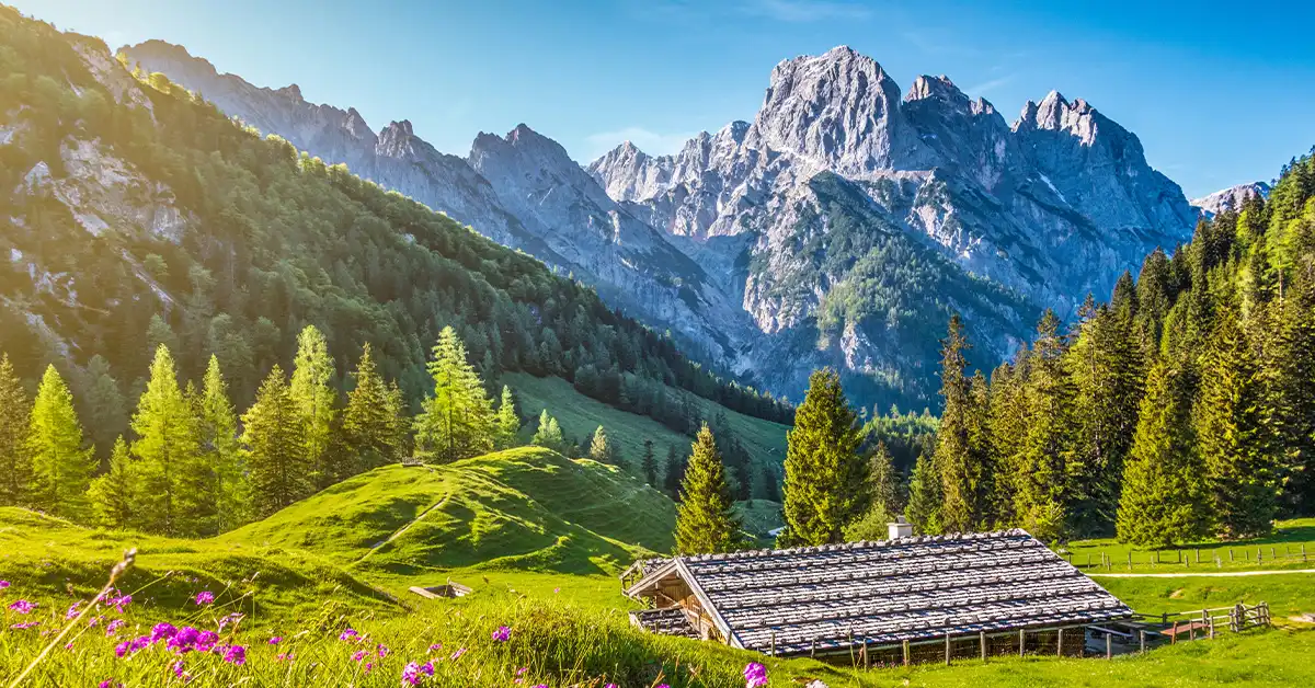 Scenic view of an alpine meadow with a rustic wooden hut and mountain peaks in Bavaria, Germany.