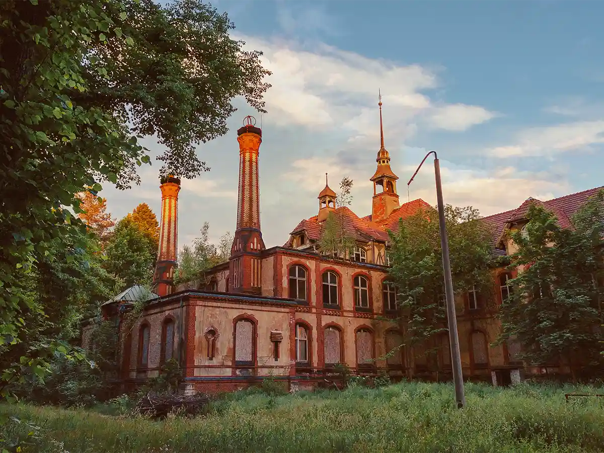 Golden-hour Beelitz-Heilstätten sanatorium, ivy-cloaked chimneys rising—haunting place to visit Brandenburg history lovers.