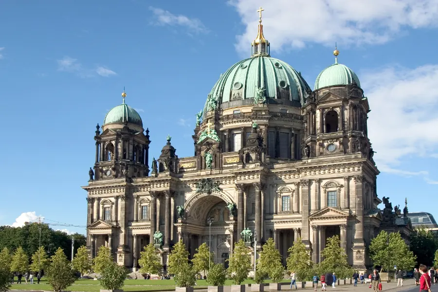 Green copper domes and gold cross of Berlin Cathedral against a blue sky