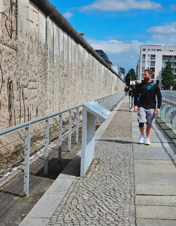Preserved section of the Berlin Wall along Bernauer Straße with an information panel and a visitor walking past