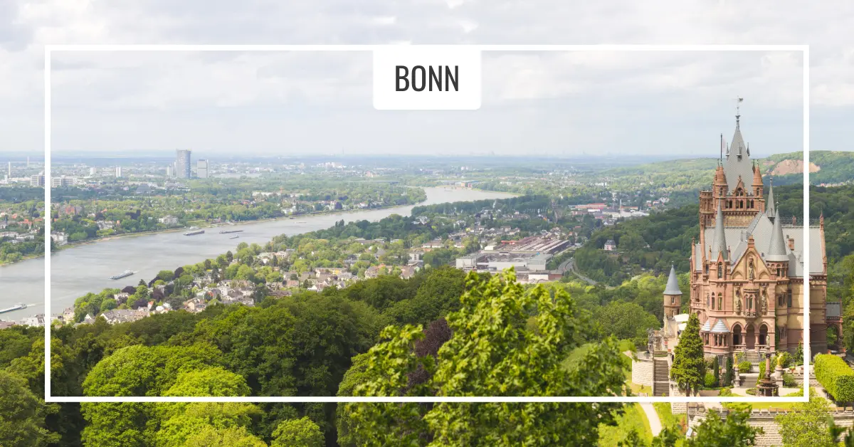 Bonn skyline with river and castle. Panoramic view of Bonn with the Rhine River flowing through the city and a historical castle-like structure surrounded by lush greenery in the foreground.
