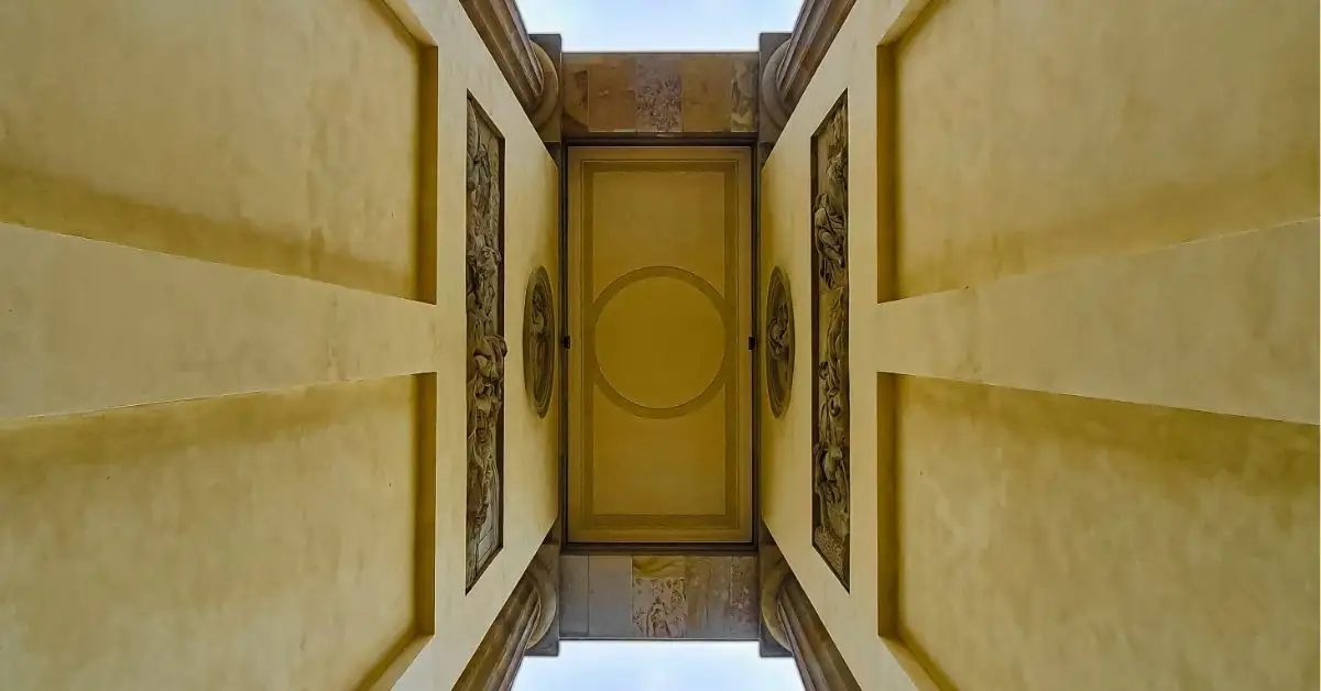Upward perspective of the ornate ceiling beneath the Brandenburg Gate, framed by classical reliefs and architectural details in golden hues.