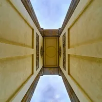 Upward view through the center columns of the Brandenburg Gate, framed by neoclassical architecture and a cloudy sky