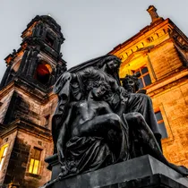Dramatic statue in front of Dresden’s historic buildings at night, lit with golden lighting against a gray sky