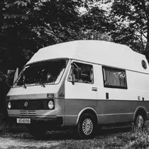 Retro-style black and white photo of a VW camper van parked under trees, giving off a nostalgic road trip vibe.