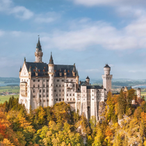 Neuschwanstein Castle perched above autumn-colored trees with sweeping views of the Bavarian countryside in the background