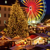 Festive German Christmas market at night with a glowing Christmas tree, wooden stalls, and a brightly lit Ferris wheel in the background