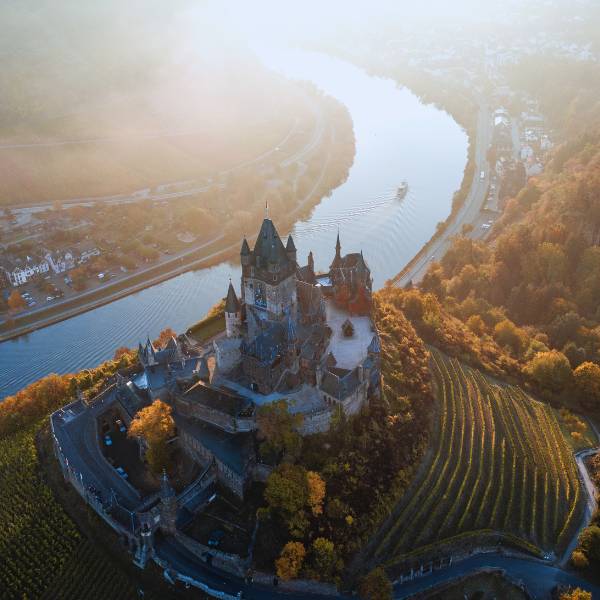 Cochem Castle is towering over the serene Mosel River! Aerial view of Cochem Castle surrounded by autumn foliage with the Moselle River winding in the background.