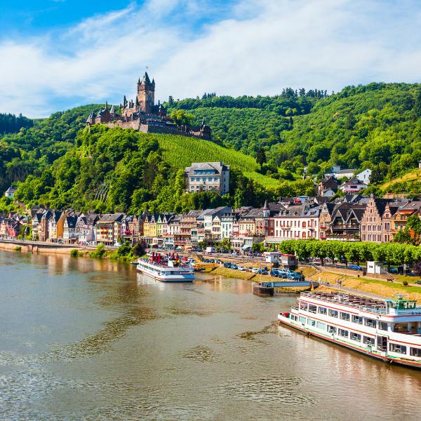 Cochem Castle on the hill with the Mosel River down below Picturesque riverside town nestled beneath the hilltop Cochem Castle, with colorful buildings lining the shore and tour boats docked along the Moselle river.