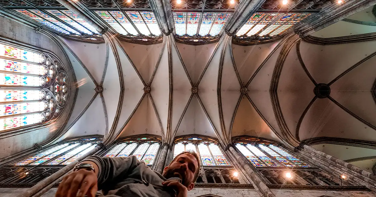 Interior view of Cologne Cathedral with soaring vaulted ceilings and stained glass windows, captured from a low angle with a Eran in the foreground.
