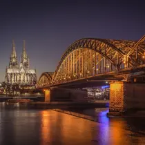 Cologne Cathedral and Hohenzollern Bridge lit up at night with reflections shimmering on the Rhine River