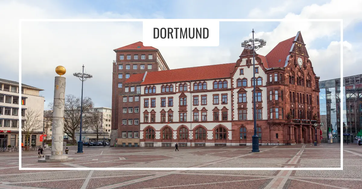 Square in Dortmund. A historical building with a red roof and ornate architecture, set in a large open square. A column with a golden sphere and modern buildings are visible in the background.