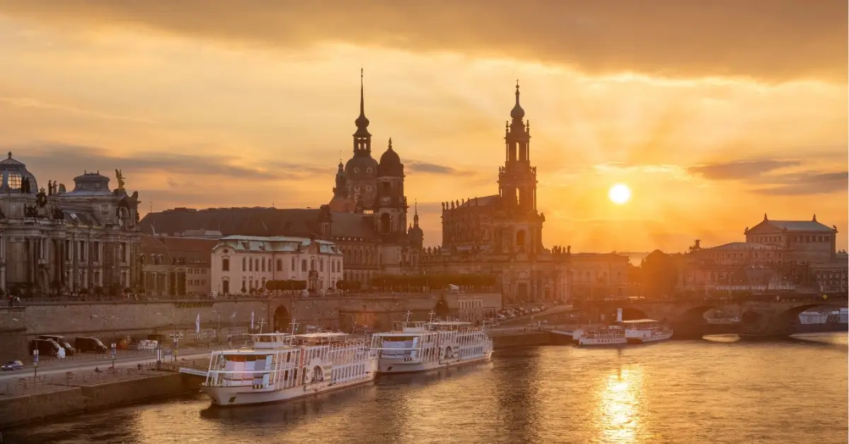 View of Dresden’s historic skyline at sunset with the Elbe River in the foreground and boats docked along the riverbank.