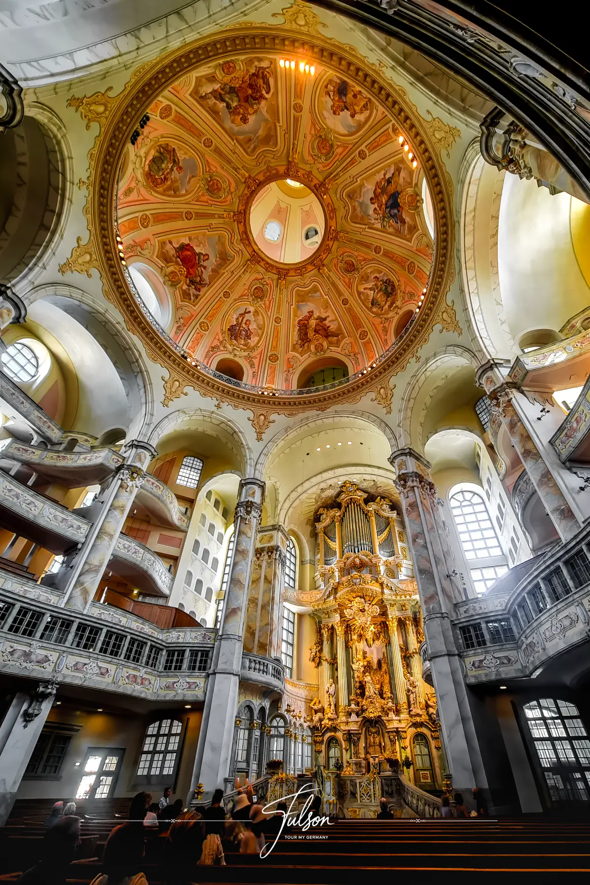 Interior of a grand dome in Dresden's Frauenkirche with intricate artwork, ornate organ, and large arched windows.