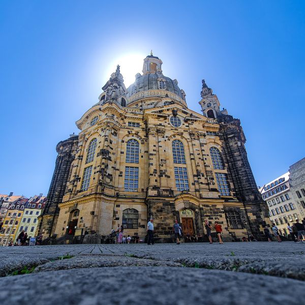 Multi-coloured stone facade of the Dresden Frauenkirche with sun shining behind it