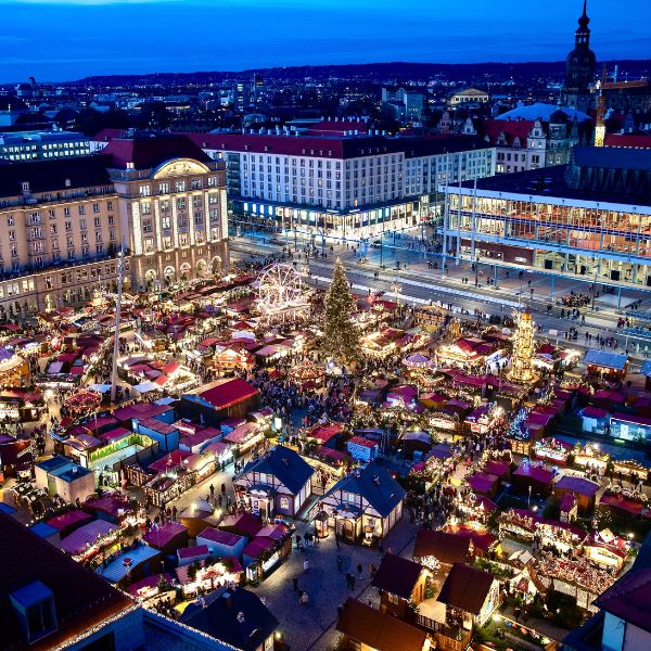 Town square filled with Christmas stalls and lights at the Dresden Striezelmarkt. Old buildings surround the square at dusk.