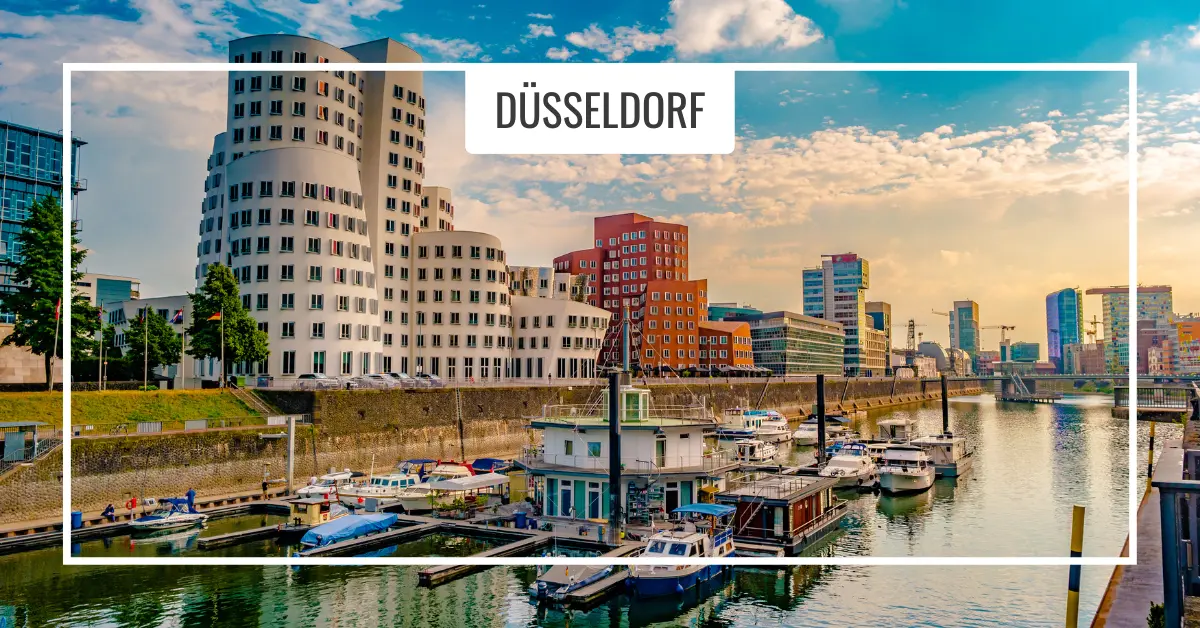 Düsseldorf skyline and river. A view of Düsseldorf, featuring modern buildings along the waterfront, small boats docked in the canal, and a partly cloudy sky.