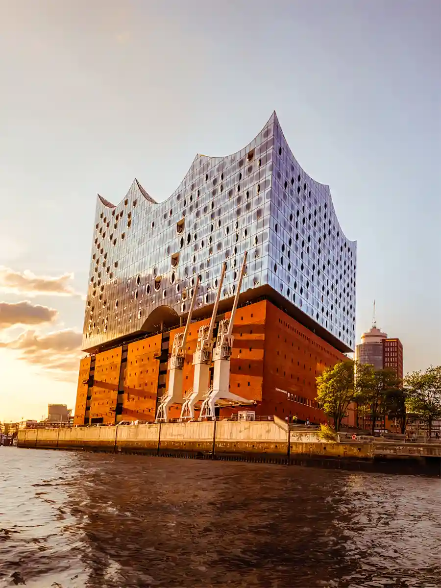 Elbphilharmonie Hamburg concert hall featuring a modern glass structure atop a historic brick warehouse, viewed from the water at sunset. Elbphilharmonie Hamburg concert hall featuring a modern glass structure atop a historic brick warehouse, viewed from the water at sunset.