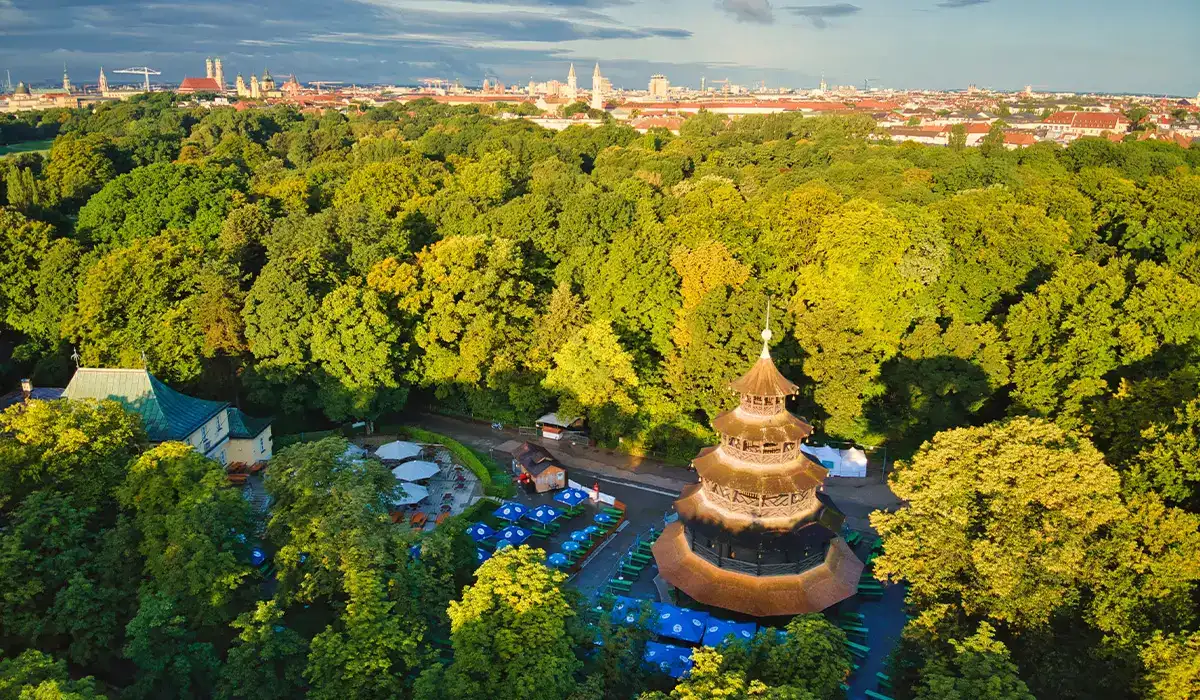Aerial view of the Chinese Tower surrounded by dense green trees and outdoor seating in the English Garden, Munich.
