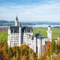 Scenic view of Neuschwanstein Castle surrounded by autumn trees with a lake and mountains in the background