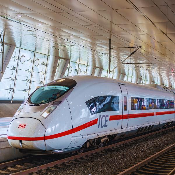 The high-speed trains at Frankfurt Central Station get you to where you need to go in a flash! A sleek white high-speed train with red accents stationed at a modern railway platform featuring an arched glass ceiling and overhead electrical lines.