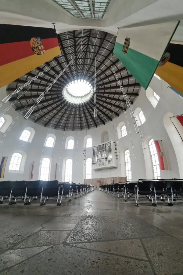Interior of St. Paul's Church in Frankfurt circular room with a domed ceiling, featuring flags, large windows, an organ, and rows of empty chairs.