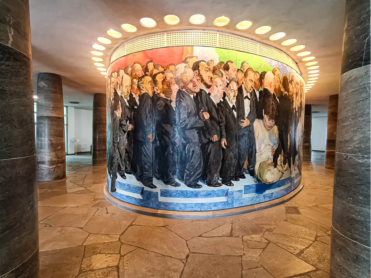 A large circular mural in St. Paul's Church, Frankfurt, depicting a crowd of formally dressed men and a child, set in a room with marble pillars and stone tile flooring.