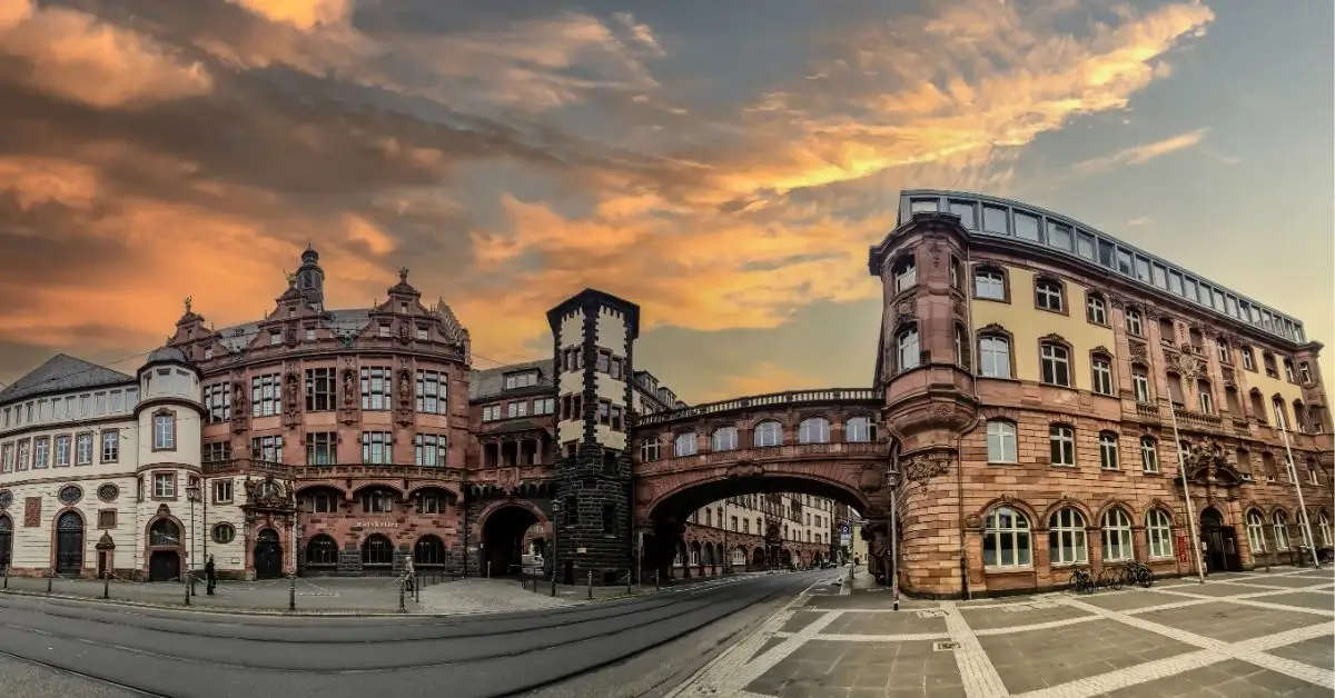 Historic stone buildings and skybridge in Frankfurt’s old town, with a dramatic sunset sky in the background.