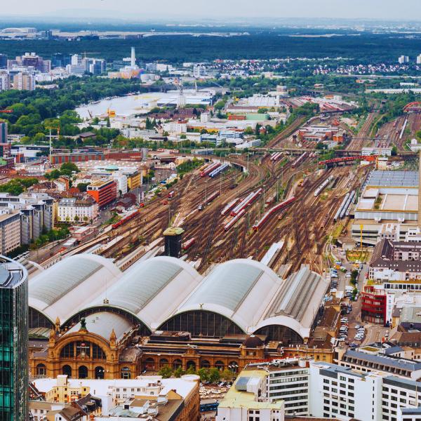Frankfurt Central Train Station Aerial view of Frankfurt Central Train Station with its distinctive arched roof, surrounded by an extensive network of railway tracks, urban buildings, and green spaces stretching toward the city skyline.