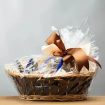 Gift basket wrapped in cellophane with a decorative brown and ivory bow, sitting on a wooden surface