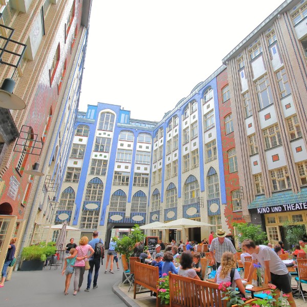 Hackescher Markt, Berlin A lively outdoor courtyard with people sitting at tables, surrounded by colorful, tall buildings with large windows.