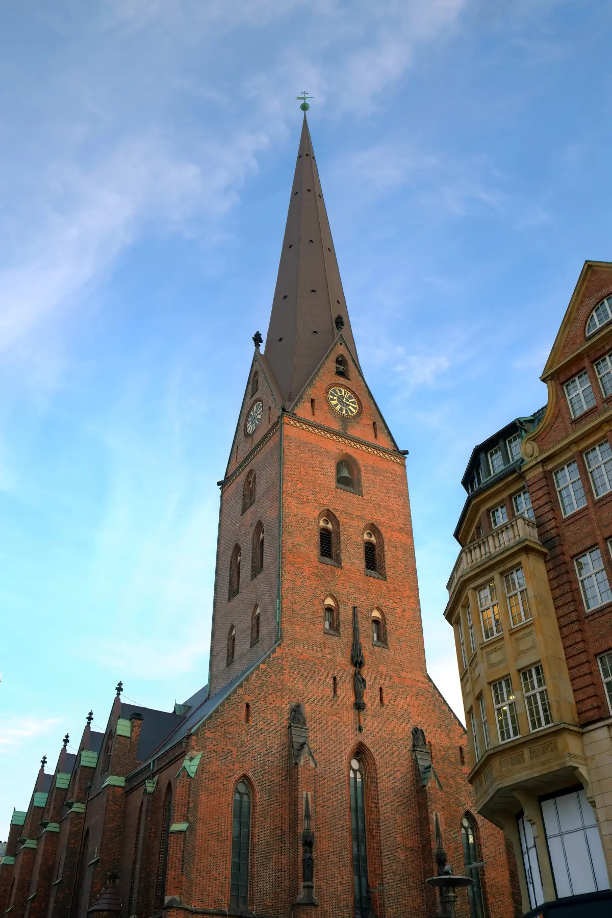 Spire on red brick church under a partly clear sky in Hamburg